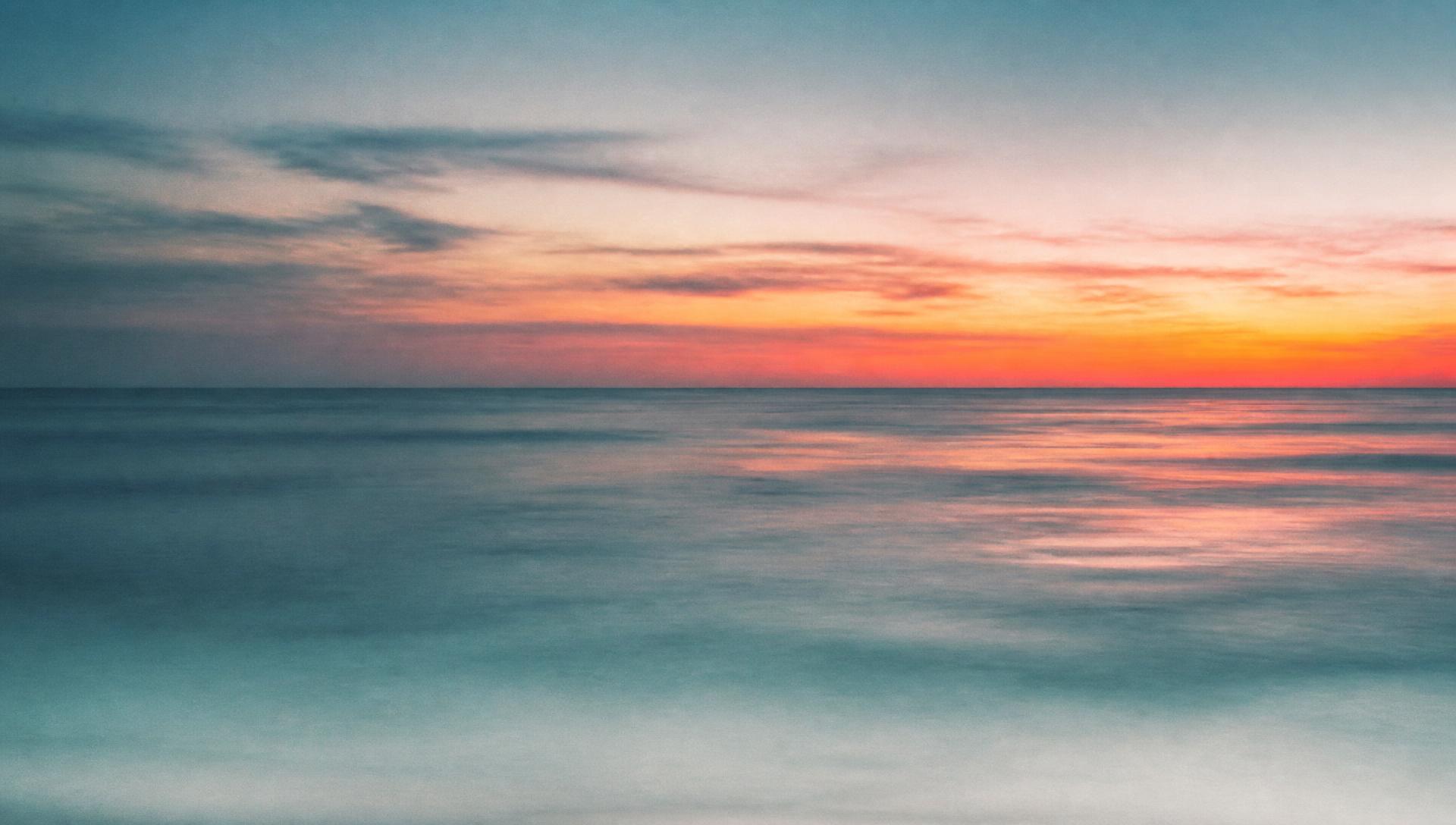 Calm open sea at sunrise with coral and amber light on the water